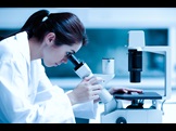 woman in lab coat looking through a microscope